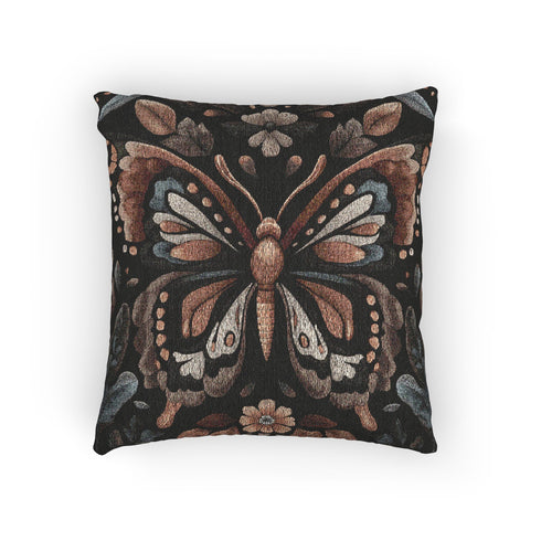 A square decorative pillow featuring an intricately detailed butterfly design in amber, gold, sage green and cream colors against a black background. The butterfly is surrounded by botanical elements with symmetrical floral patterns.
